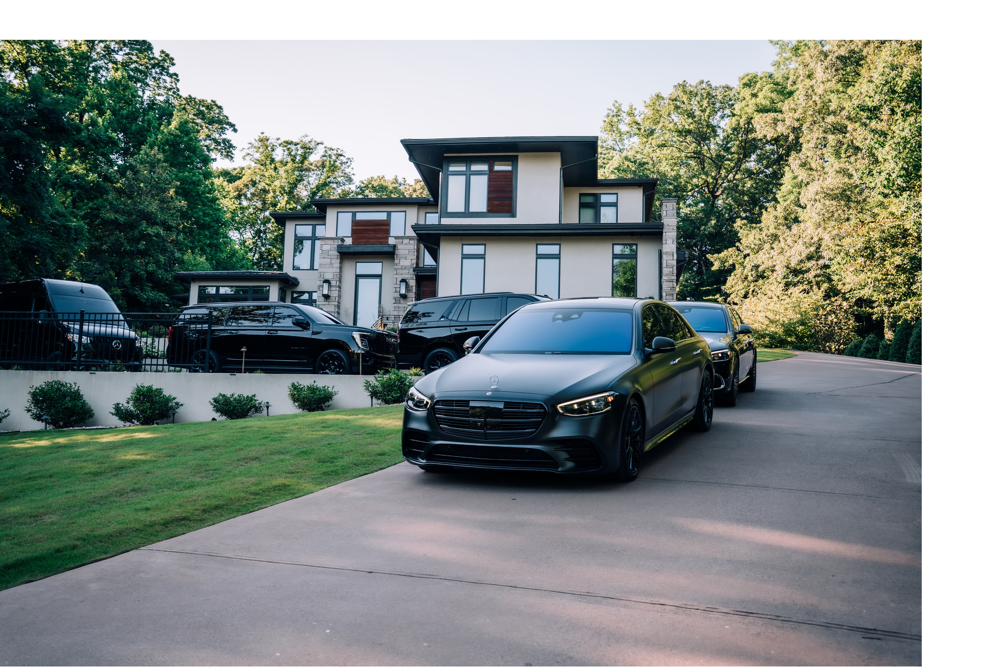 Matte black Mercedes-Benz S-Class parked on a driveway in front of a modern luxury mansion.