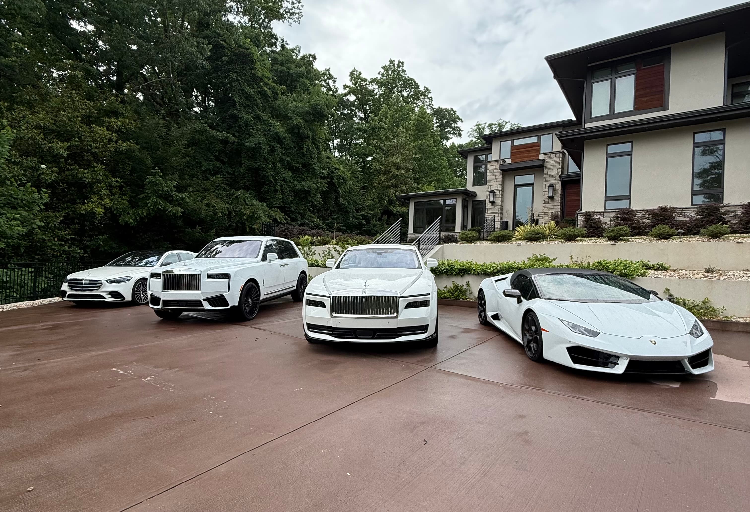 Four white luxury cars, including a Lamborghini and Rolls-Royce, parked in front of a mansion.