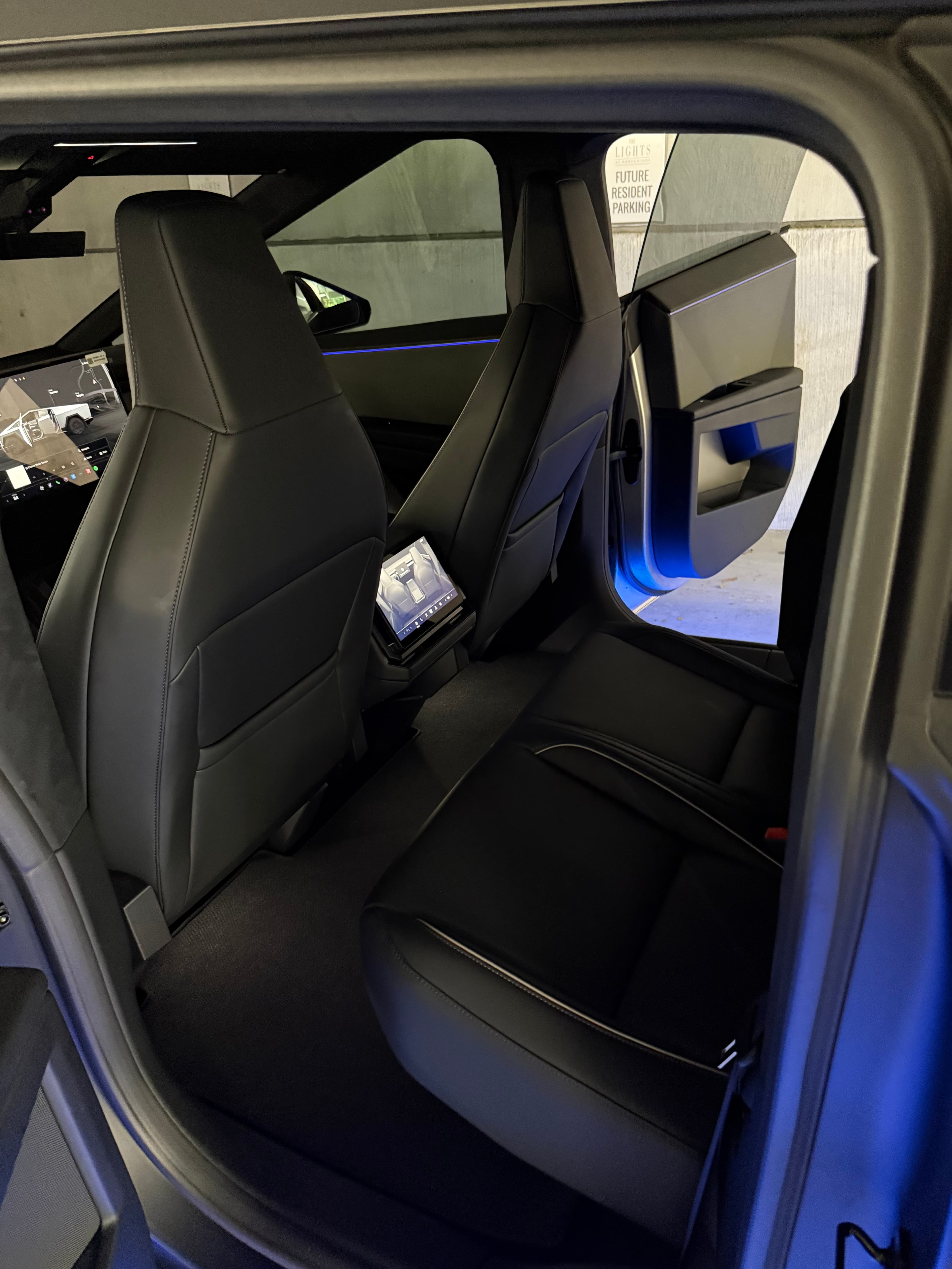 Rear interior of a Tesla Cybertruck featuring black seats, a touchscreen, and blue lighting.
